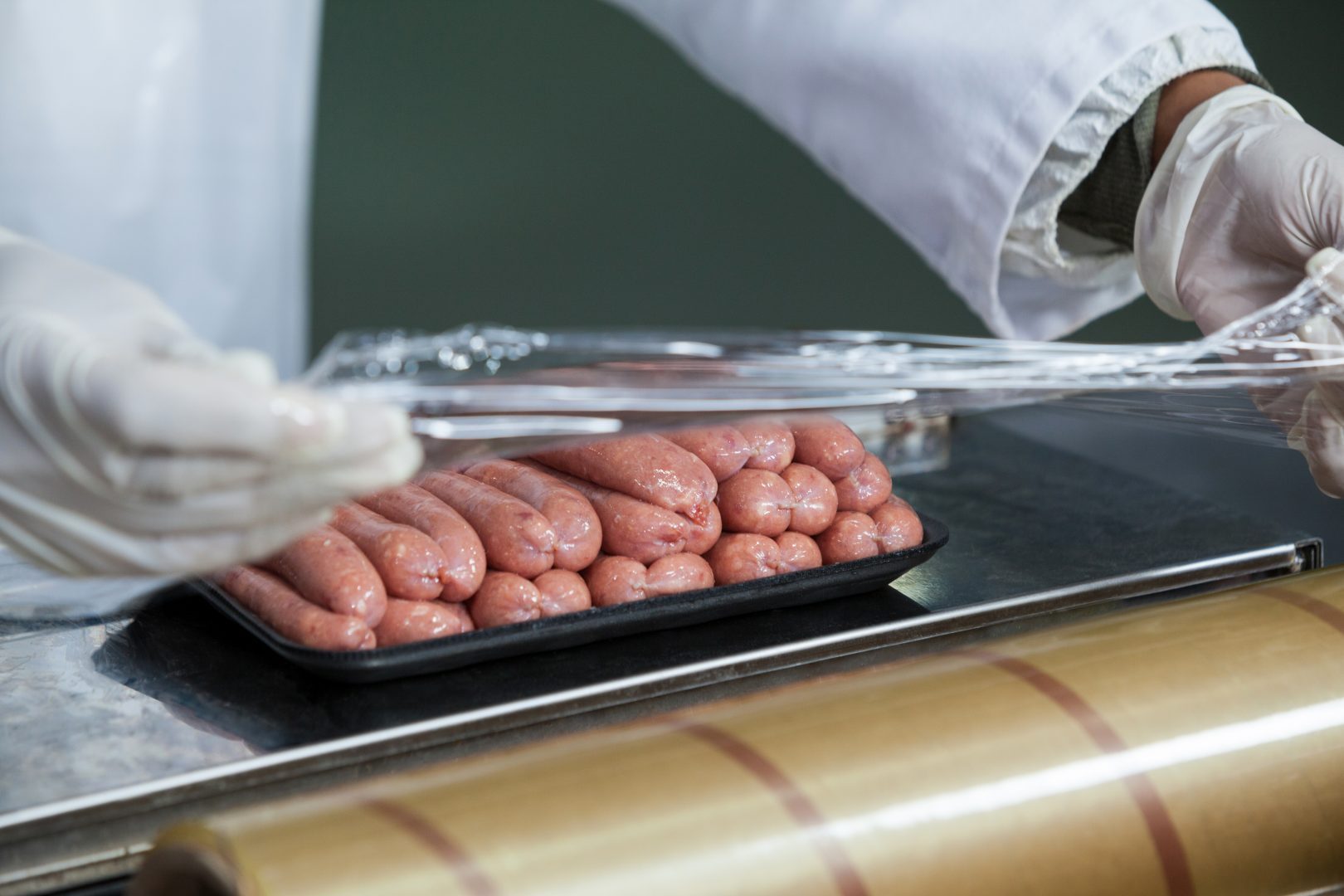 Close-up of butcher packing raw sausages at meat factory.